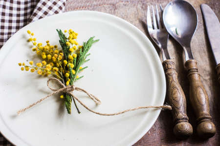 Spring festive dining table setting with yellow mimosa flowers, napkins and vintage cutlery on a white wooden boardの写真素材