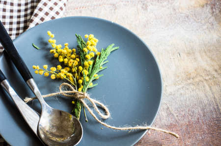 Spring festive dining table setting with yellow mimosa flowers, napkins and vintage cutlery on a white wooden boardの写真素材