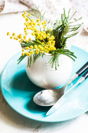 Spring festive dining table setting with yellow mimosa flowers, napkins and vintage cutlery on a white wooden boardの写真素材