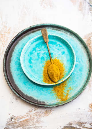 Yellow curry spice on vintage spoon and bright turquoise platesの写真素材