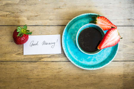 Turquoise cup of coffee and fresh strawberries with good morning noteの写真素材