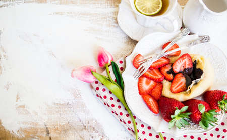 Breakfast time with fresh strawberries, chocolate and crepes on rustic backgroundの写真素材