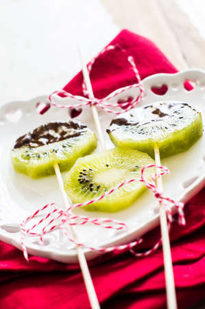 Fruit dessert with fresh kiwi fruit slice in chocolate on heart-shaped plateの写真素材