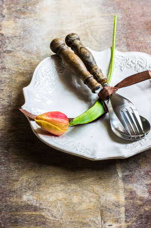 Rustic table setting with bright tulip flower, silverware and plate on old wooden table. View from above with copy spaceの写真素材