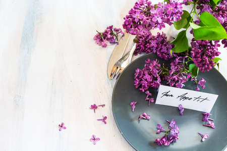 Spring time table setting with lilac flowers and vintage plates and silverware on rustic wooden tableの写真素材