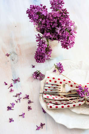 Spring time table setting with lilac flowers and vintage plates and silverware on rustic wooden tableの写真素材
