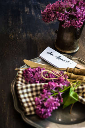 Spring time table setting with lilac flowers and vintage plates and silverware on rustic wooden tableの写真素材