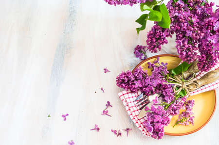 Spring time table setting with lilac flowers and vintage plates and silverware on rustic wooden tableの写真素材