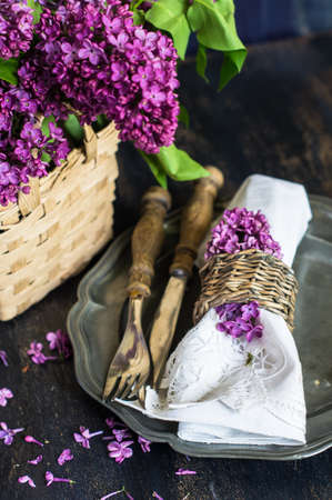 Spring time table setting with lilac flowers and vintage plates and silverware on rustic wooden...