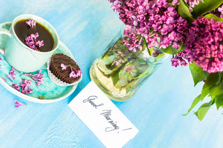 Lilac flowers and cup of coffee with good morning note on rustic wooden background