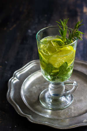 Summer drink with ice, mint, rosemary and lime on rustic tableの写真素材
