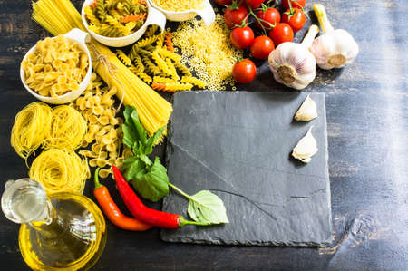 Pasta cooking concept with  basil, tomatoes,  pepper chili, garlic and pasta on vintage wooden backgroundの写真素材