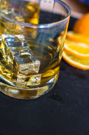 Glass of wiskey, lemon and ice on rustic wooden tableの写真素材
