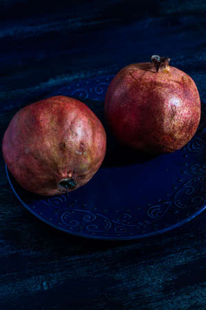 Fresh pomegranate fruit on vintage plate on rustic wooden tableの写真素材