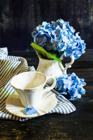 Vintage style table setting with fresh blue hydrangea flowers on rustic wooden tableの写真素材
