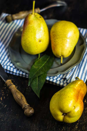 Fresh organic pears on vintage plate with rustic napkin on old wooden kitchen table