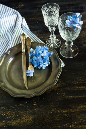 Vintage style table setting with fresh blue hydrangea flowers on rustic wooden tableの写真素材