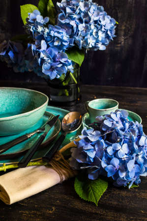 Vintage style table setting with fresh blue hydrangea flowers on rustic wooden tableの写真素材