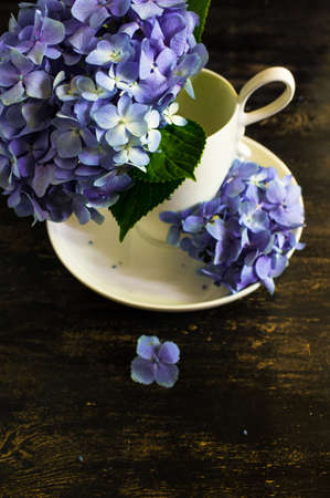 Vintage style table setting with fresh blue hydrangea flowers on rustic wooden tableの写真素材