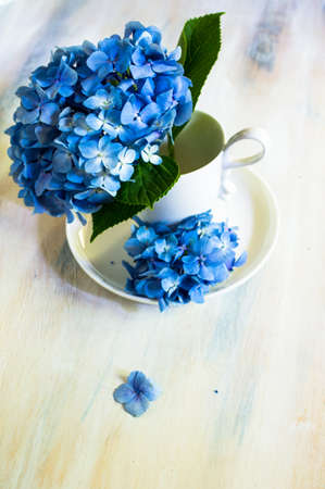Vintage style table setting with fresh blue hydrangea flowers on rustic wooden tableの写真素材