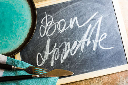 Bon appetite on a chalkboard with rustic silverware and napkin