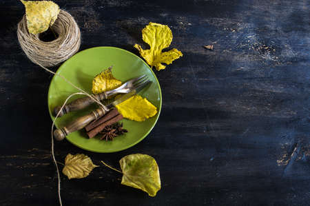 autumnal table setting with yellow leaves and vintage plates and silverware on dark rustic tableの写真素材
