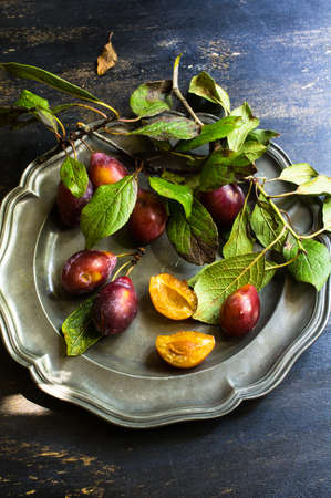 Fresh organic plums with leaves on old rustic wooden tableの写真素材