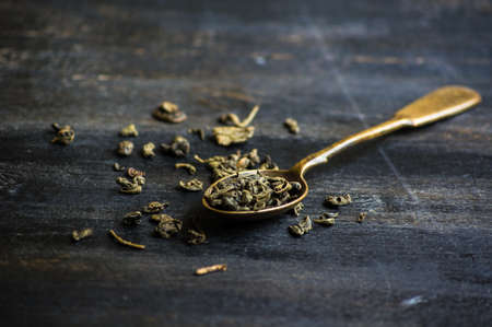 Vintage tea spoon with green tra leaves on dark wooden table with copy spaceの写真素材