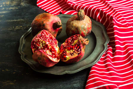 Ripe pomegranate on the vintage plate on dark rustic wooden table with copyspaceの写真素材