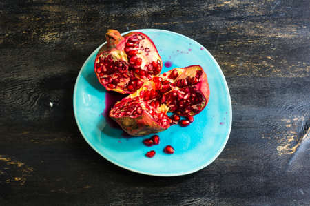Ripe pomegranate on the vintage plate on dark rustic wooden table with copyspaceの写真素材
