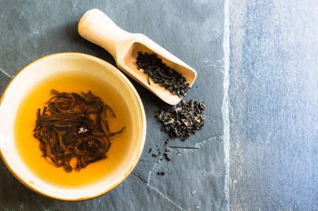 Cup of black tea and wooden spoon with tea leaves on rustic wooden table with copyspaceの写真素材