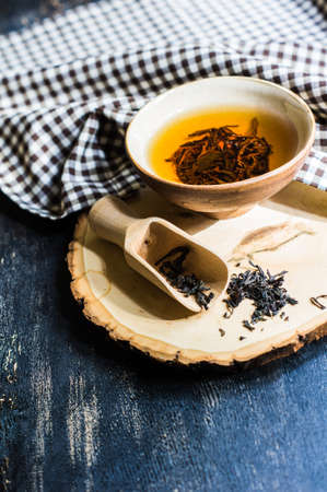 Cup of black tea and wooden spoon with tea leaves on rustic wooden table with copyspace