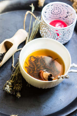 Cup of black tea with cinnamon and lavender, wooden spoon with tea leaves on rustic wooden table with copyspaceの写真素材