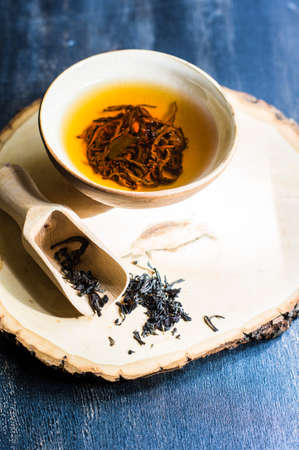 Cup of black tea and wooden spoon with tea leaves on rustic wooden table with copyspaceの写真素材