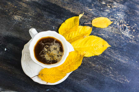 Cup of coffee with bright yellow leaves on rustic wooden table with copyspaceの写真素材