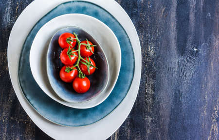 Fresh ripe organic cherry tomatoes and bright ceramic plates on dark wooden table wt copyspaceの写真素材
