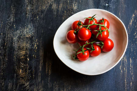 Fresh ripe organic cherry tomatoes and bright ceramic plates on dark wooden table wt copyspaceの写真素材