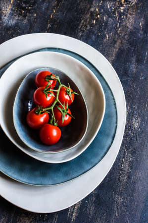 Fresh ripe organic cherry tomatoes and bright ceramic plates on dark wooden table wt copyspaceの写真素材