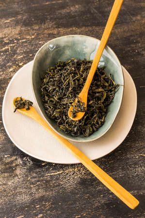 Dried green tea leaves in a ceramic bowl on dark wooden backgroundの写真素材