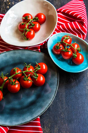 Fresh ripe organic cherry tomatoes and bright ceramic plates on dark wooden table wt copyspaceの写真素材