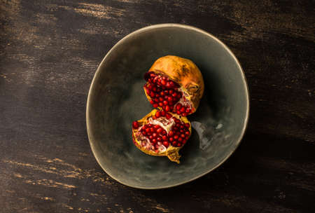 Ripe organic pomegranate fruits on bright plates on dark rustic wooden tableの写真素材