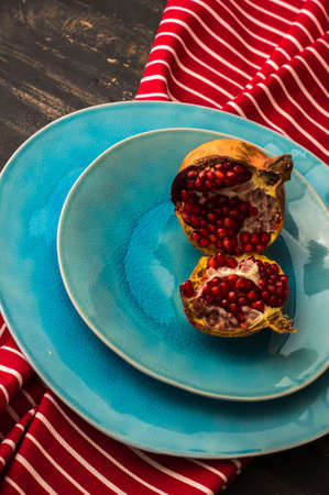 Ripe organic pomegranate fruits on bright plates on dark rustic wooden tableの写真素材