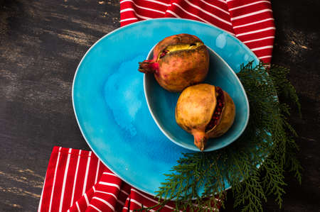 Ripe organic pomegranate fruits on bright plates on dark rustic wooden tableの写真素材
