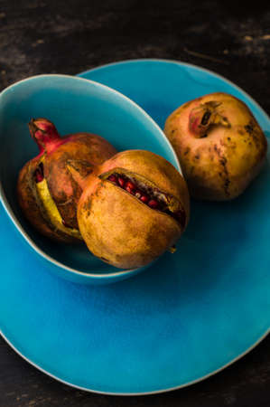 Ripe organic pomegranate fruits on bright plates on dark rustic wooden tableの写真素材