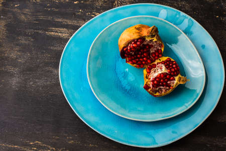Ripe organic pomegranate fruits on bright plates on dark rustic wooden tableの写真素材