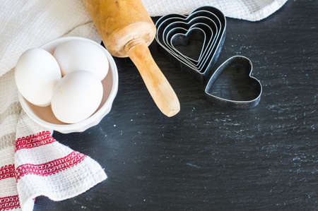 Baking concept for St. Valentines Day with heartshaped cutters and eggs on dark wooden table with copyspaceの写真素材