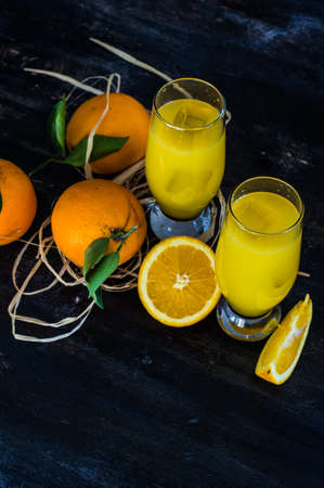 Glass of orange juice with straw and ripe orange fruits with green leaves on dark rustic wooden tableの写真素材