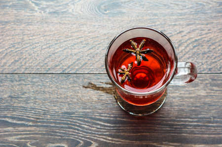Glass of mulled wine with spices like an anise star and cinnamon sticks on dark wooden backgroundの写真素材