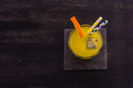 Glass of orange juice with straw and ripe orange fruits with green leaves on dark rustic wooden tableの写真素材