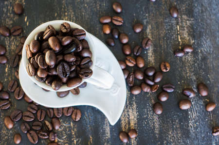 Vintage coffee mug with raw coffee beans on dark rustic wooden background